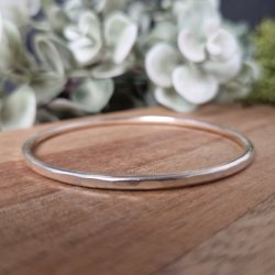 Sterling silver hammer texture bangle made from 3mm recycled silver wire resting on a wooden base with green foliage in the background