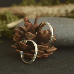 Sterling Silver hoop earrings with stamping details displayed on a fir cone with a natural grey stone in the background