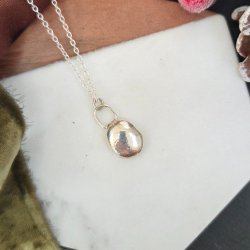 Organic silver pebble pendant on a silver chain displayed on a marble coaster with a green velvet ribbon and festive berries and fir cones