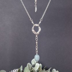 A molten link suspended from a belcher chain against a black background.  A wrapped loop drop is suspended from the link with an aquamarine nugget at the end.  To the top of the picture you can see the ornamental extender with faceted aquamarines.  Green 