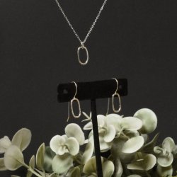 Sterling silver oval pendant and matching earrings set against a black background with green foliage towards the bottom