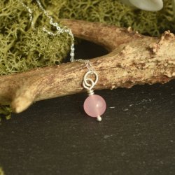 A simple, delicate pink rose quartz 10mm bead necklace on a sterling silver chain.  Displayed against a natural background on a black slate slab.
