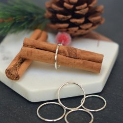 A minimalist, hammer textured sterling silver band shown on a cinnamon stick.  There are various other sizes of ring displayed in the foreground and festive props in the background