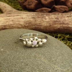 Sterling silver ring with pink cubic zirconia set in a bezel surrounded by molten silver balls.  The band is a half round profile.  Shown on a grey stone with natural antler, green moss and a fir cone in the back ground
