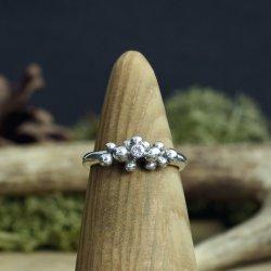 A purple 2.5mm cubic zirconia, bezel set and nestled between organic, molten silver balls of granulation sitting on a natural wooden display stand with natural moss in the background