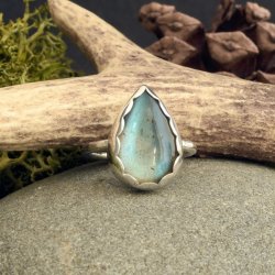 Handmade sterling silver labradorite ring with a pear-shaped blue stone, scalloped bezel, and hammered band, displayed on a stone with natural props.