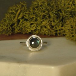 This labradorite and sterling silver ring is laying on a marble base with natural green moss in the background.  The setting is clearly visible